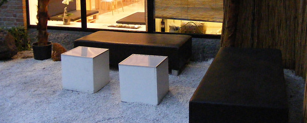 Moderner Außenbereich mit schwarzen Sitzbänken, weißen Würfeltischen und Kiesboden.